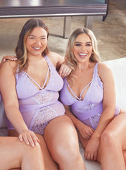 Two women wearing matching lavender lingerie sitting on a couch.