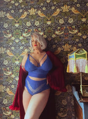 Person wearing a blue lingerie set with a red robe against a decorative wall.