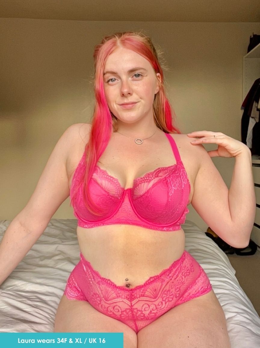 Woman wearing a pink bra and underwear set in a bedroom setting.