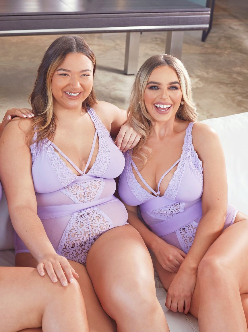 Two women wearing matching lavender lingerie sitting on a couch.