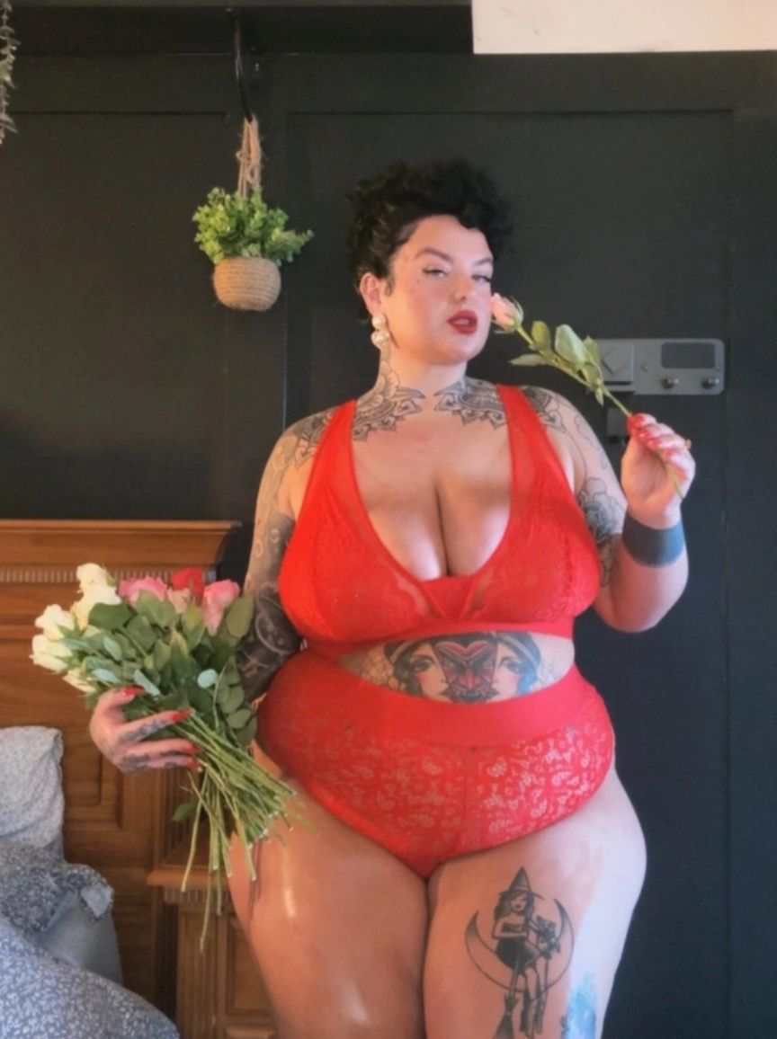 Person wearing the chilli pepper red Hallie Bralette & Brazilian Set holding flowers indoors.